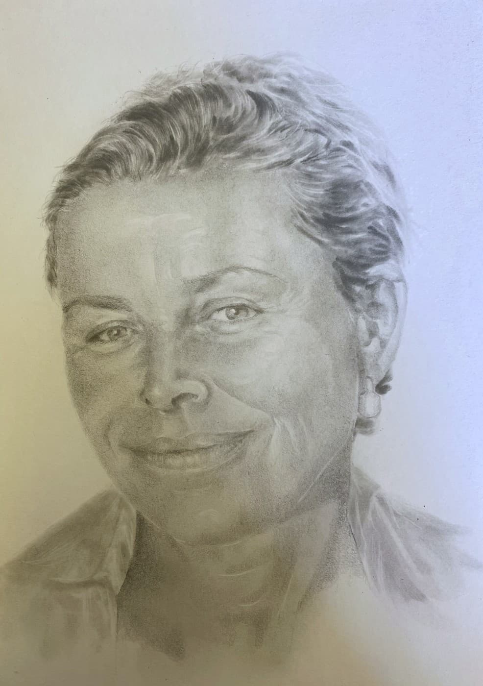 Pencil portrait of a smiling woman with short hair and an earring.